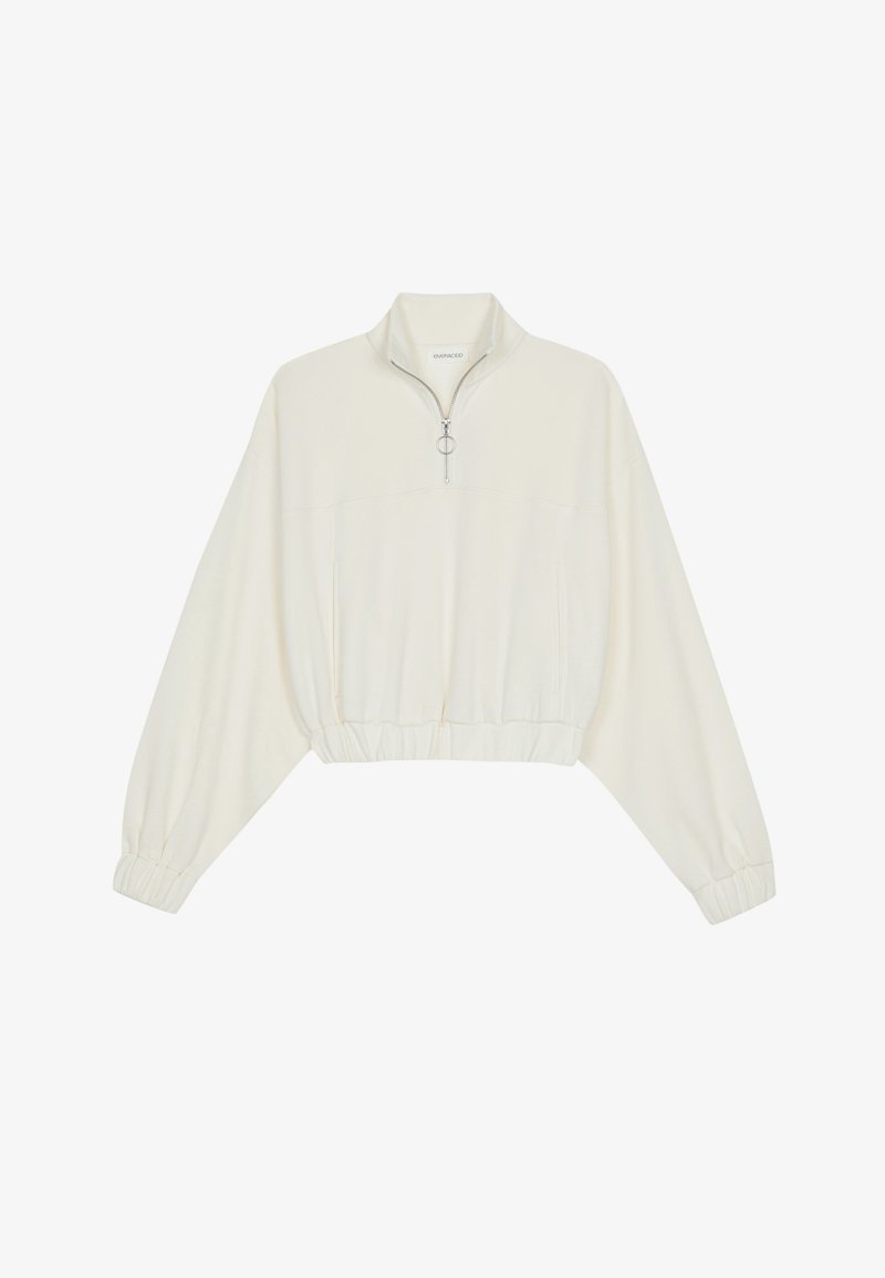 Kratka pulover v kremnem blagu, z visokim ovratnikom, pol-zadrgo, elastičnim robom in manšetami, z gladko teksturo in minimalističnim oblikovanjem.