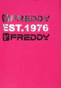 T-shirt in cotone rosa con stampa nera e argento metallizzato "FREDDY" e "EST. 1976", dalla texture liscia e design semplice.