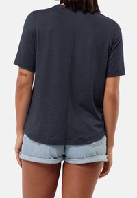 Navy short-sleeve T-shirt with a rounded neckline, soft texture, and a central back seam. Worn with rolled-up denim shorts.