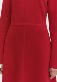 Rode gebreide jurk met lange mouwen, een aansluitend lijfje en een rechte snit. Naadtoesparingen geven structuur aan het totale ontwerp.