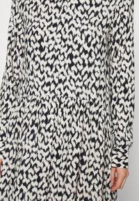Långärmad klänning i lätt material, med ett svartvitt abstrakt mönster, rynkad midja och manschettärmar.