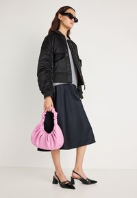 Sort bomberjakke med rynkede ærmer, grå sweater, mørkeblå nederdel, pink pungtaske og sorte slingback-sko med spids tå.