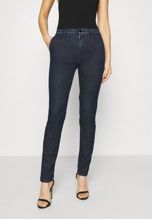 Jean en denim bleu foncé, coupe slim, avec un design classique à cinq poches, passants de ceinture et détails de couture subtils. Texture lisse, sans motifs.