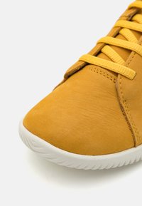 Żółte zamszowe sneakersy z okrągłym noskiem, kontrastującą gumową podeszwą i płaskimi sznurówkami. Gładka faktura z detalami szwów wzdłuż boków.