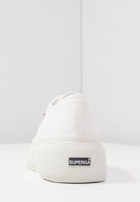 Białe płócienne sneakersy z teksturowaną gumową podeszwą, o zaokrąglonym kształcie, minimalistycznym designie i czarnym logo Superga na pięcie.