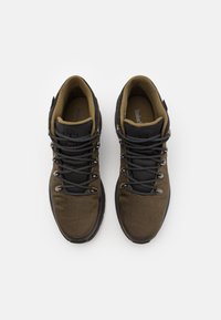 Zapatos de senderismo en marrón oscuro y negro, con una parte superior de malla texturizada, cordones resistentes y un collarín acolchado para mayor soporte. Marca Timberland visible.