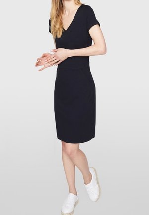 Vestido azul marino con escote en V, mangas cortas, cintura ajustada, falda hasta la rodilla y bolsillos. Combinado con zapatillas blancas.