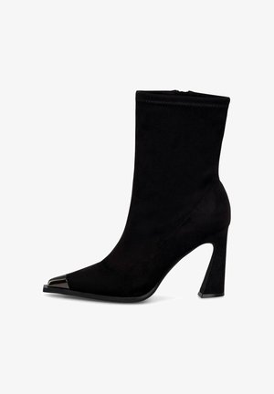 Stivale alla caviglia nero in morbida suede con punta affusolata e accentuazione metallica sulla punta. Caratterizzato da un tacco alto e chunky e dettagli cuciti.
