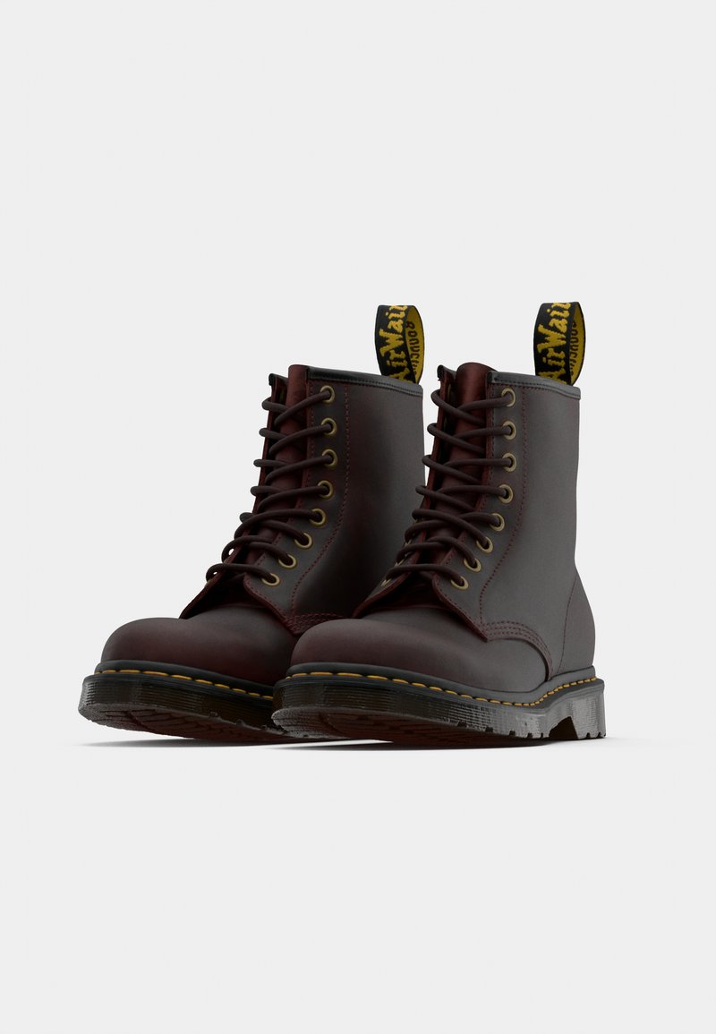 Bottes en cuir marron à lacets avec un bout arrondi, des coutures jaunes et une languette de tirage avec un texte noir. Semelle en caoutchouc avec un motif texturé.
