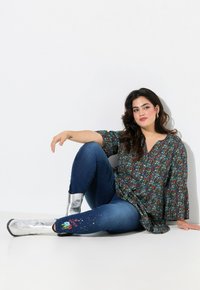Blusa de estampado floral con mangas acampanadas, combinada con jeans azul oscuro con flores bordadas y botas de tobillo plateadas.