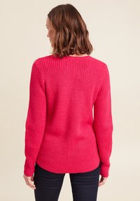 Strickpullover in leuchtendem Pink mit geripptem Textur, langen Ärmeln und Rundhalsausschnitt. Von hinten mit lockerer Passform betrachtet.