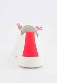 Sneaker bianco caratterizzato da un materiale testurizzato, con un accento rosso sul tallone e lacci rossi. La suola è leggermente testurizzata per una migliore aderenza. Design minimalista.