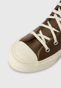 Brūnie ādas sporta apavi ar baltu gumijas uzgali, apaļiem acu caurumiem un kontrastējošām krēmkrāsas šņorēm. Strukturēts zole ar dimantu rakstu detaļām.