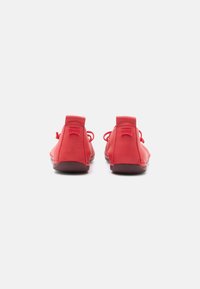 Red leather shoes with a low profile, rounded toe, and pull tabs at the heel. Features a textured finish and laces for secure fit.