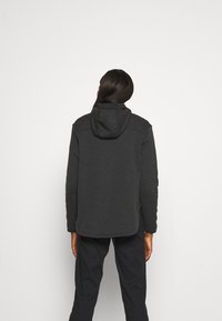 Dunkelgraue Fleecejacke mit Kapuze, die einen lässigen Schnitt, flache Nähte und eine glatte Textur aufweist. Schlichtes Design, keine sichtbaren Logos oder Verzierungen.