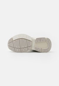 Helle Sneaker-Sohle mit strukturiertem Gummi für Grip, mit ausgeprägten Profilmustern sowie Branding in der Mitte und im Fersenbereich.