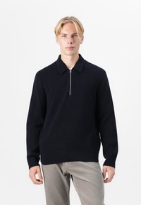 Tumedast sinise värvi kudumipullover ribitud tekstuuriga, millel on kaelus ja lühike esine tõmblukk, paired heledate pükste jaoks.