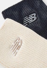 Dos diademas de punto, una en azul marino oscuro con un logotipo negro, y otra en crema con un logotipo beige, que muestran patrones texturizados.