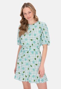 Blå gingham kjole med pufærmer. Har blomster- og bladmønstre, en elastisk talje og en flæset kant. Lavet af bomuldsstof.