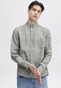 Camicia grigia a maniche lunghe con bottoni, realizzata in tessuto leggero, con colletto, bottoni frontali e un piccolo logo sul petto.