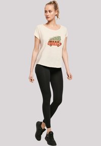 Crème korte mouwen t-shirt met een kleurrafische afbeelding van een vintage bus met een kerstboom, gecombineerd met zwarte leggings en zwarte schoenen.