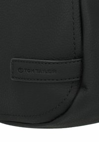 Sac à main en cuir noir avec une finition texturée. Présente une couturière et une petite étiquette de marque embossée. Design compact et arrondi.