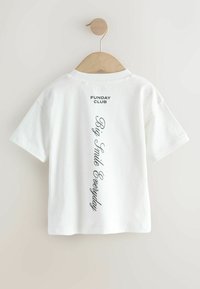 White cotton t-shirt hanging on a wooden hanger. Features short sleeves, a round neck, and printed text "FUNDAY CLUB" and "Big Smile Everyday" on the back.