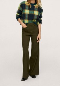 Wełniany sweter w zielono-żółtą kratę zestawiony z dopasowanymi, wysokim stanem oliwkowozielonymi spodniami. Czarne botki na kostkę dopełniają stylizację.