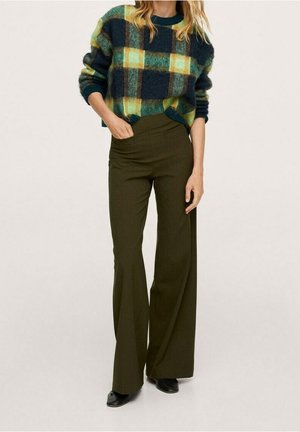 Groen- en geelgeruit wollen trui gecombineerd met hooggetailleerde, nauwsluitende olijfgroene broek. Zwarte enkellaarsjes maken de look af.