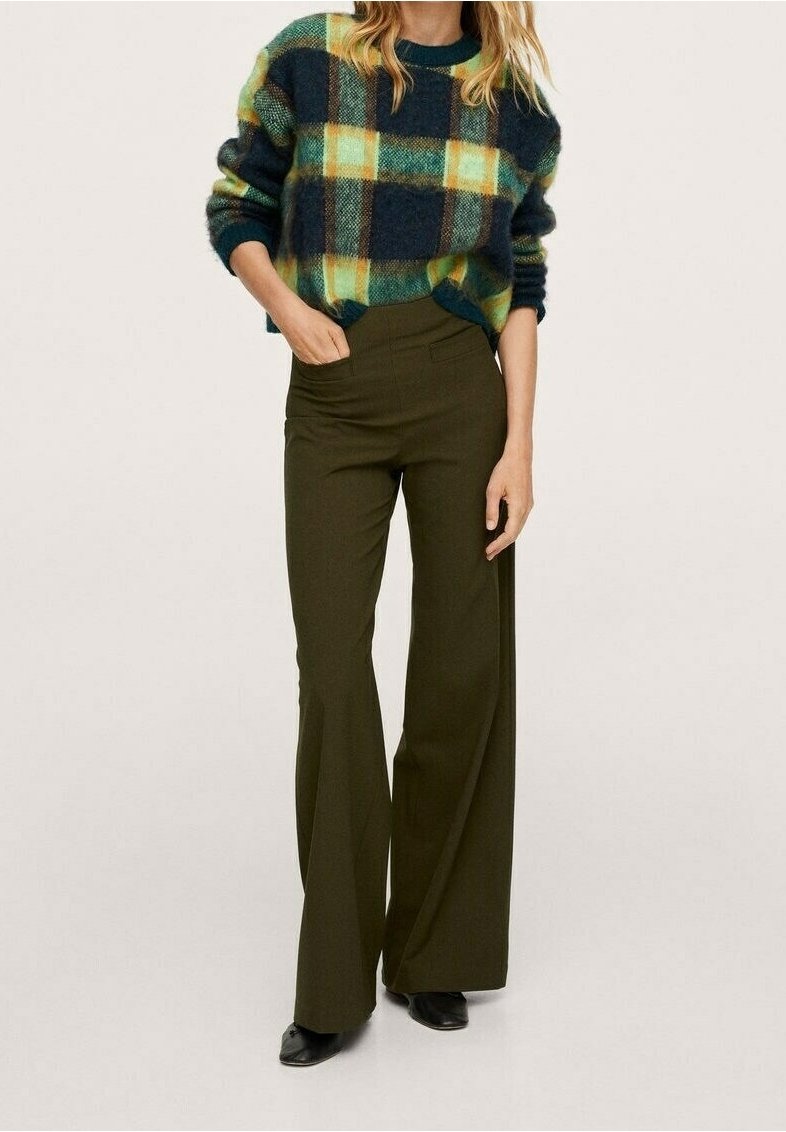 Wełniany sweter w zielono-żółtą kratę zestawiony z dopasowanymi, wysokim stanem oliwkowozielonymi spodniami. Czarne botki na kostkę dopełniają stylizację.