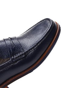 Mocassin en cuir bleu marine avec finition texturée, un embout mocassin cousu, un design épuré et une semelle brune contrastante.