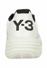 Zapatilla blanca con acentos negros y gran logotipo "Y-3" en el talón. Presenta una suela texturizada y un material superior suave.