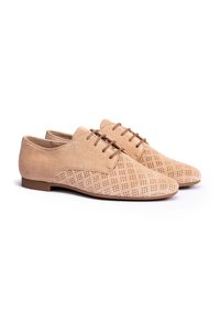 Des chaussures en suède beige à lacets avec un design perforé, featuring une pointe arrondie et une semelle plate, sur fond blanc.