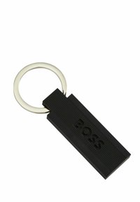 Zwarte rubberen sleutelhanger met een geribbeld textuur en een reliëflogo; voorzien van een zilveren metalen sleutelringbevestiging.