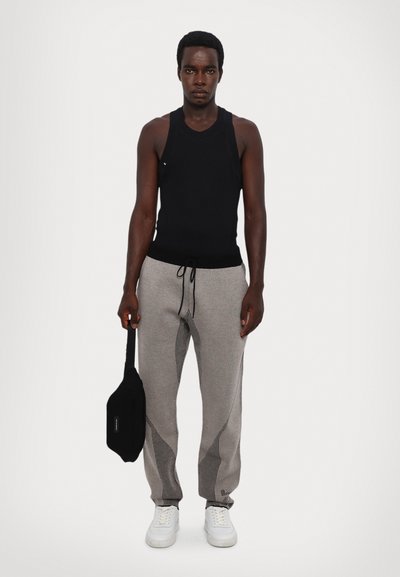 Black tank top, gray patterned joggers with drawstring, white sneakers, and a small black bag. Model standing against a plain background.