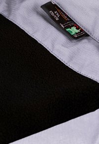 Schwarzer Fleece-Stoff mit einem grauen Abschnitt; beinhaltet ein Etikett mit der Größe XXL und ein Design mit einem grünen Frosch. Weiche Textur, warme Ausstrahlung.