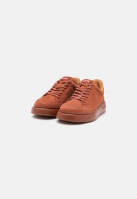 Sneaker in suede marrone con suola ammortizzata, design arrotondato e chiusura con i lacci. Etichetta logo rossa sulla linguetta e fodera interna a contrasto.