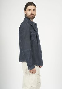 Mörkblå denimskjorta med långa ärmar, knappstängning, framficka och texturerad yta, tillsammans med ljusa cargobyxor.