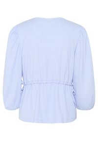 Ljusblå, texturerad blus med puffärmar, rund nacke och elastisk midja. Har sidoflätor för justerbar passform.