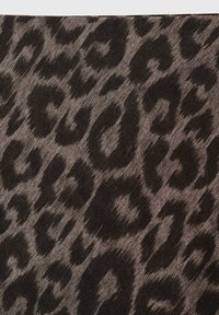 Tkanina s leopardjim vzorom v odtenkih črne in bež, z teksturirano površino, neenakomernimi pikami in mehkobnim videzom.