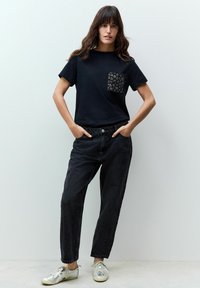 T-shirt nera in cotone con tasca a fantasia, abbinata a jeans in denim scuri a vita alta e scarpe da ginnastica metalliche. Design semplice e casual.