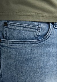 Pantalones vaqueros de mezclilla en azul claro con un diseño clásico de cinco bolsillos; cuentan con costuras en el bolsillo delantero y un botón negro en la cintura.