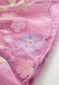 Rózsaszín, áttetsző szövet, amelyen különböző árnyalatú rózsaszín és lila virágok hímzése található, fodros szélekkel és finom textúrával.