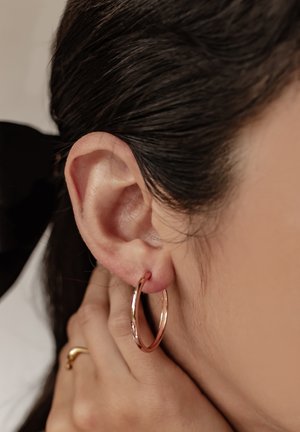 Roségold-Hoops mit glattem, poliertem Finish in einem durchstochenen Ohr getragen, mit rundem Design. Nahaufnahme von Ohr und Ohrring.