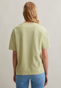 T-shirt di cotone verde chiaro con vestibilità comoda, maniche corte e collo a coste. Design semplice senza motivi o accenti visibili.