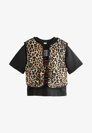 Vesta s leopardím vzorom s dvoma prednými vreckami, nosená cez čierne tričko s grafickým potlačou. Vesta má okrúhly výstrih a viazanie.