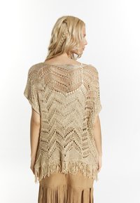 Top de ganchillo color beige con un patrón en zigzag y dobladillo de flecos, hecho de hilo texturizado. Corte holgado, mangas cortas y diseño de espalda descubierta.