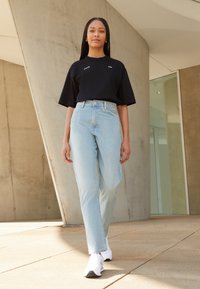 T-shirt oversized preto com letras brancas, jeans de cintura alta azul-claro e ténis brancos; tecido suave, ajuste descontraído e corte reto.