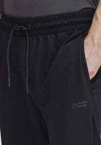 Zwarte sportbroeken met een elastische tailleband en een trekkoord. Voorzien van een logo aan de zijkant en een zachte, gladde stoftextuur.
