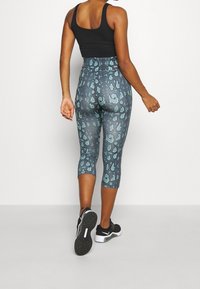 Top nero, leggings Capri stampati in teal e grigio con motivo leopardato e scarpe da ginnastica nere con suola bianca.